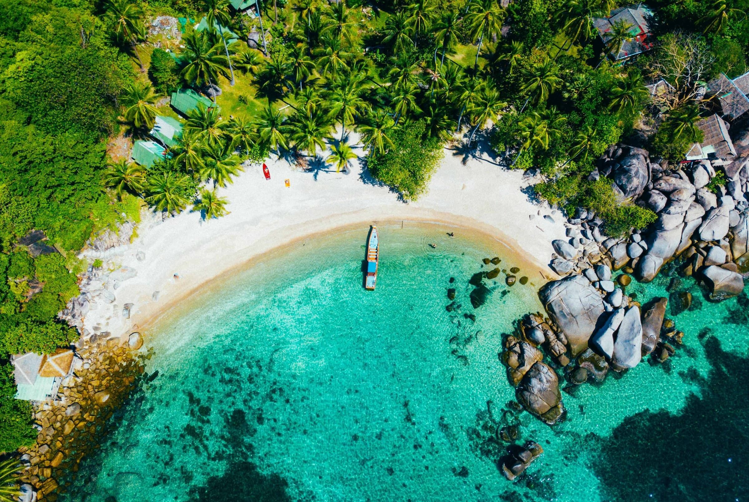Aerial view of a sandy cove with turquoise water and granite boulders