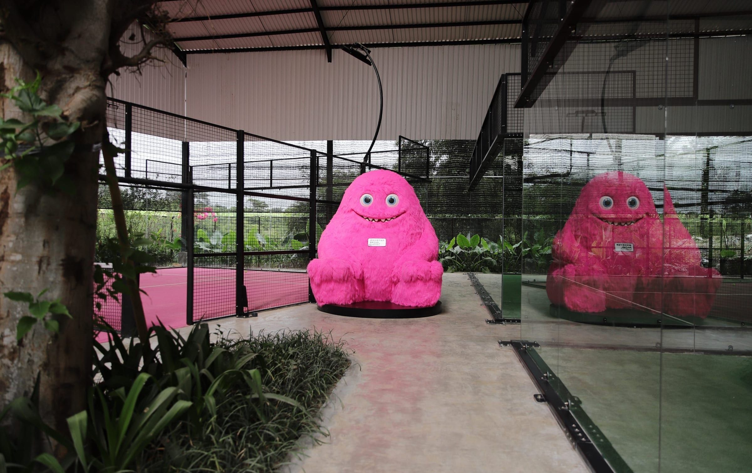 Giant pink monster mascot on a covered padel court at Monster Padel