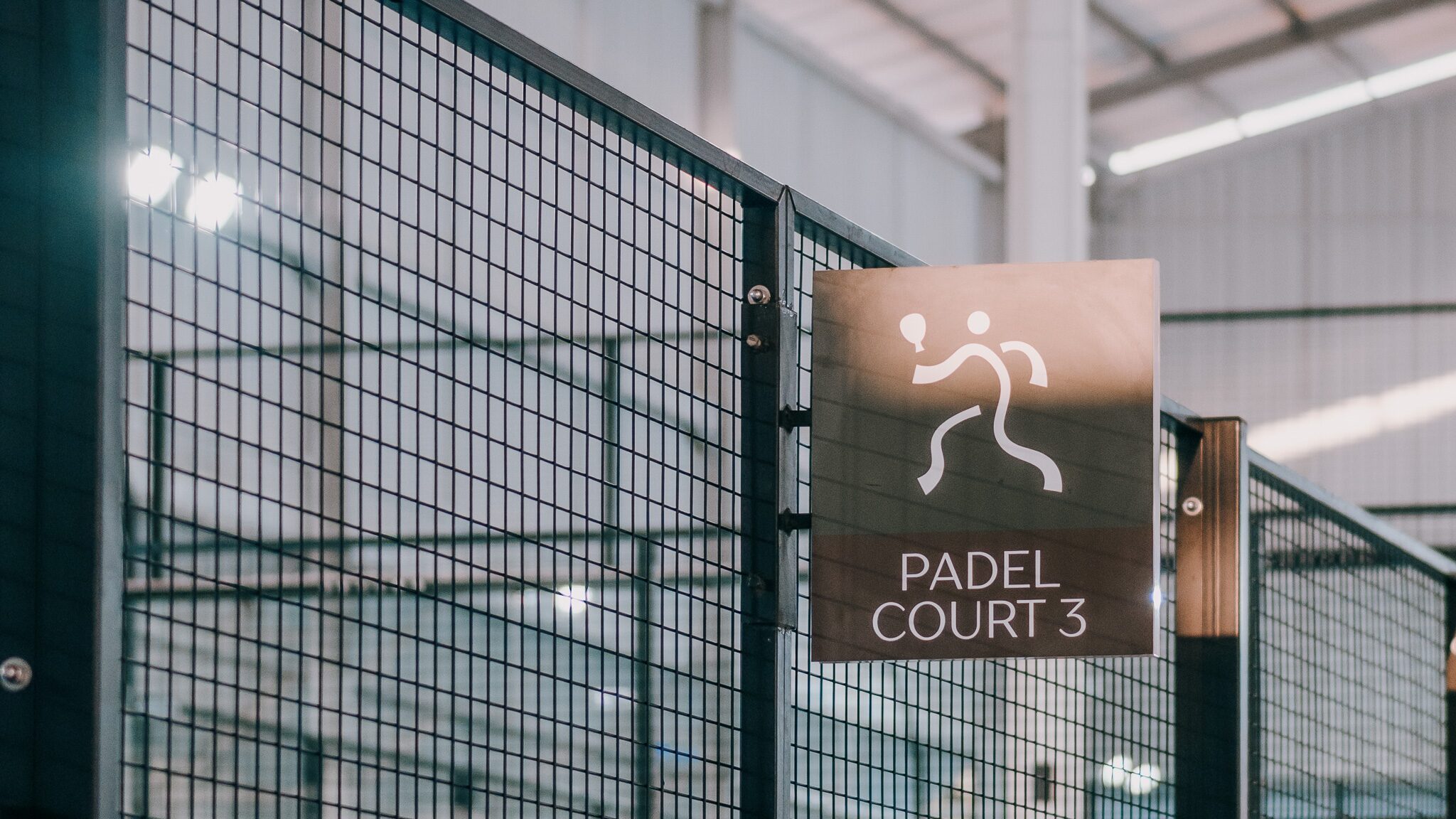 A “Padel Court 3” sign on the mesh fence of a covered padel court