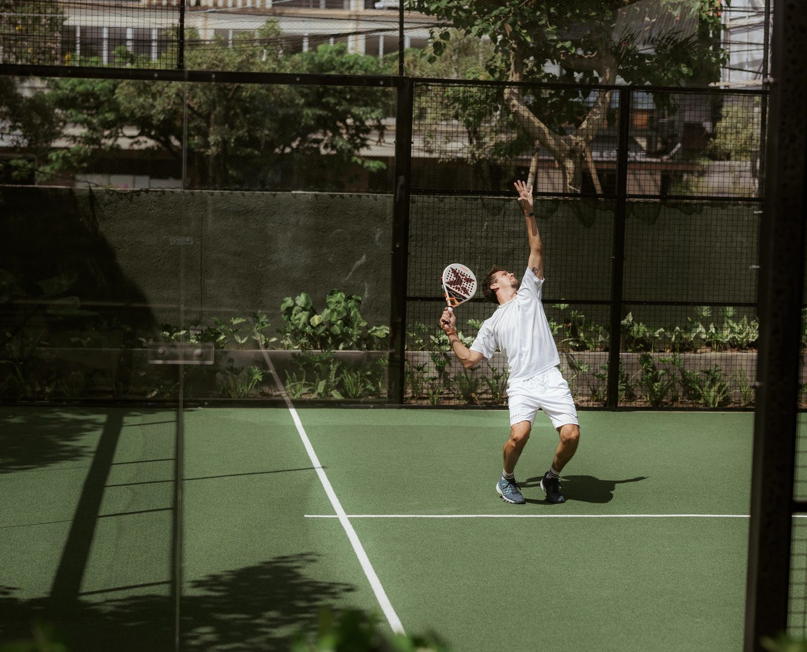 A padel player serving on an outdoor court