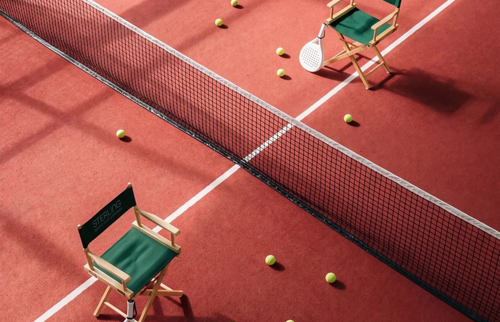 Two green director's chairs, rackets and balls on a red court, seen from above