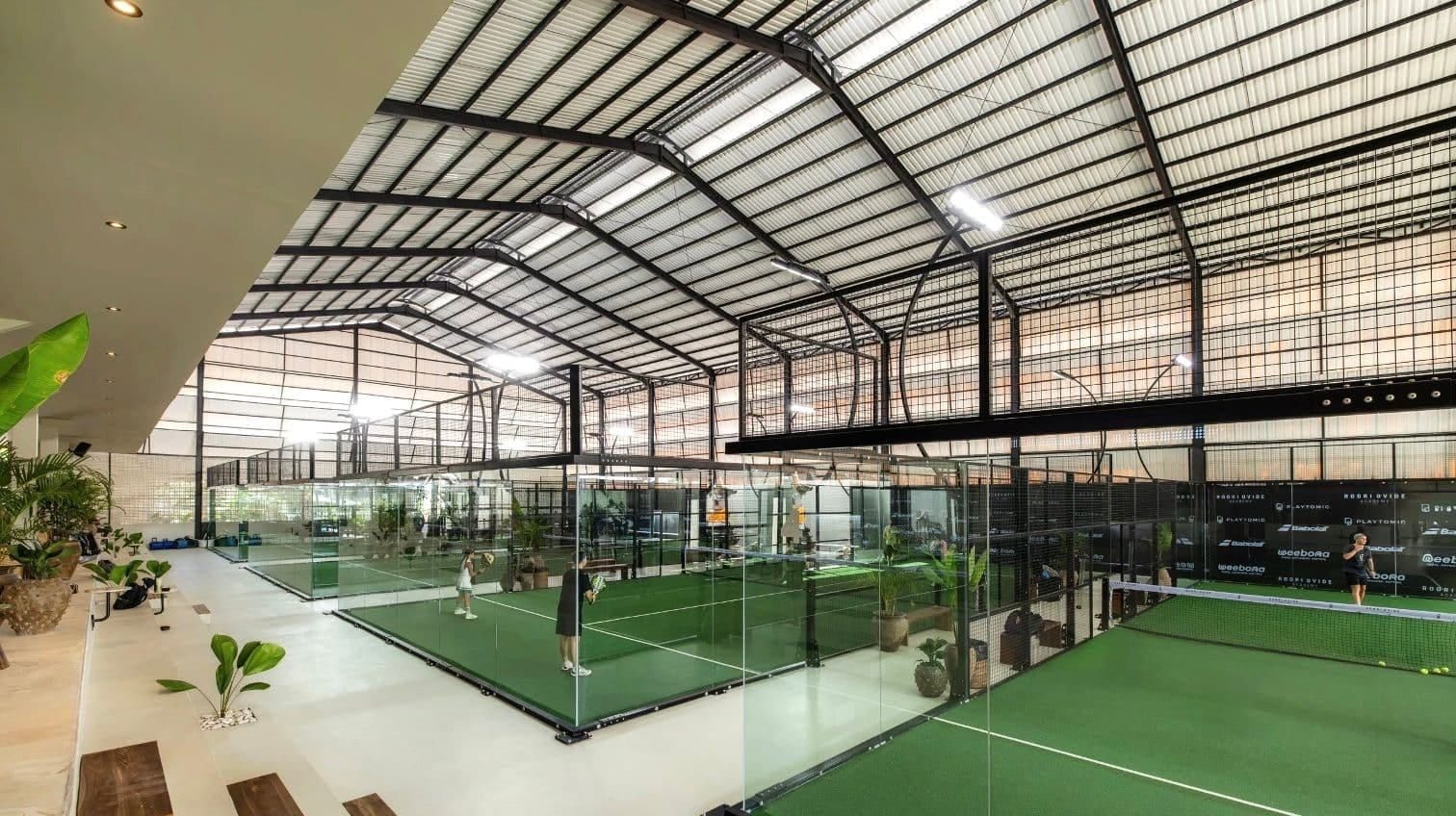 Rows of glass-walled courts under a high roof at TAO Padel Academy